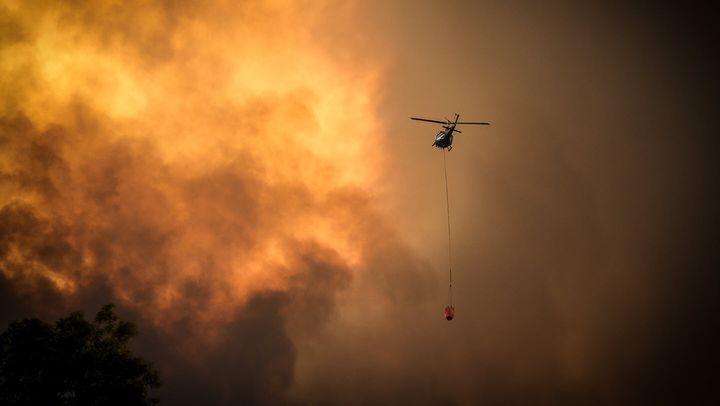 Helicopters dump water on bushfires as they approach homes located on the outskirts of the town of Bargo on December 21, 2019